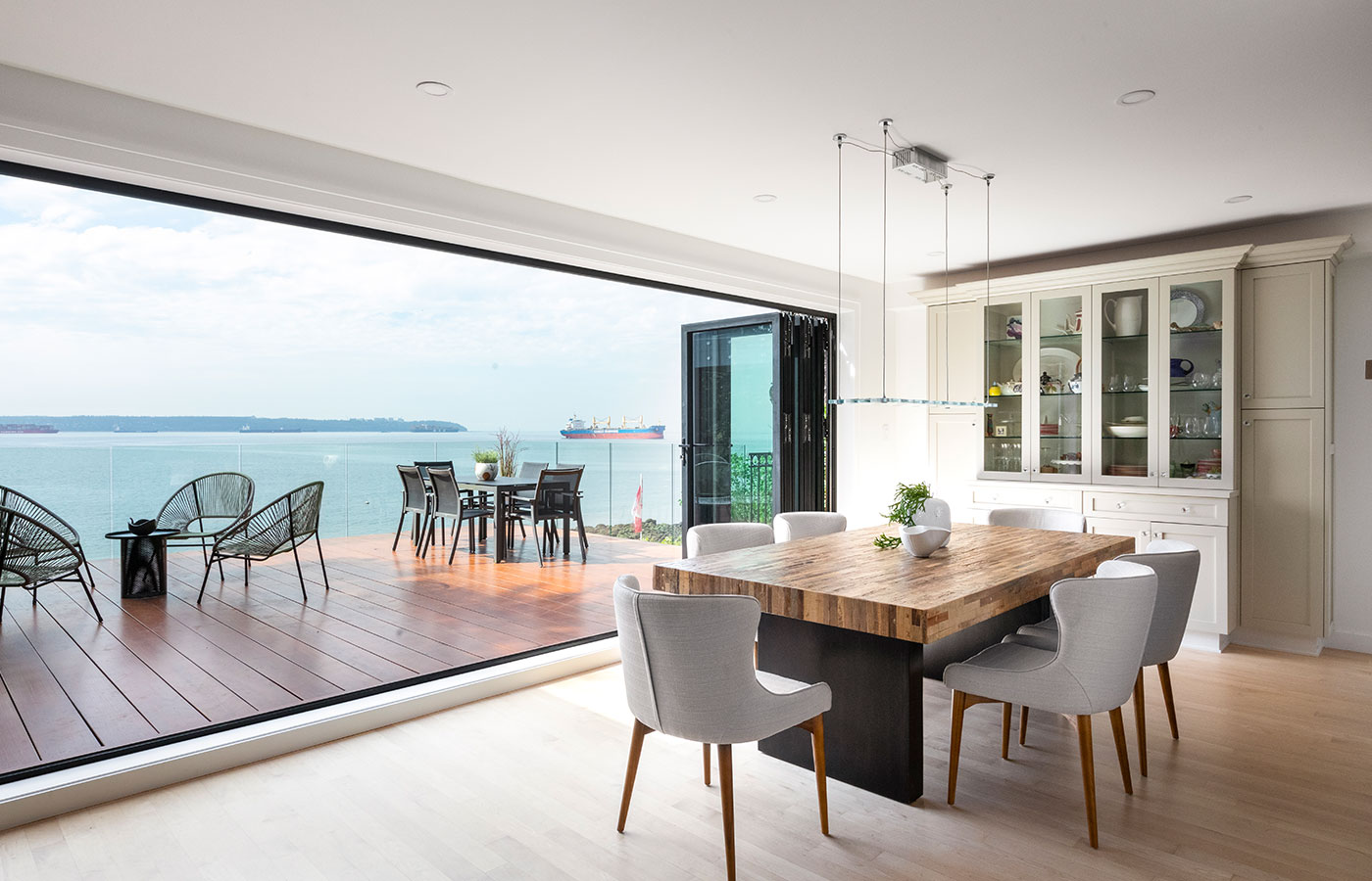 modern dining room with huge horizontal glass window to the left overlooking large balcony and Pacific Ocean in West Vancouver