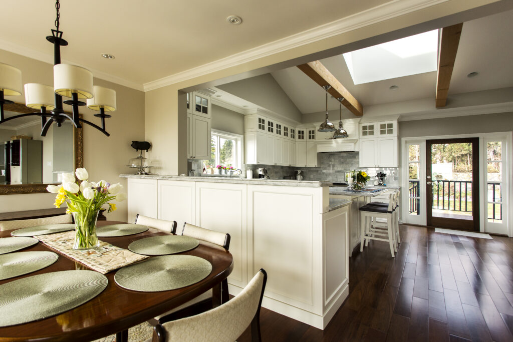 Open-concept kitchen renovation with white cabinets, skylights, exposed wood beams, breakfast bar, and adjoining dining area.