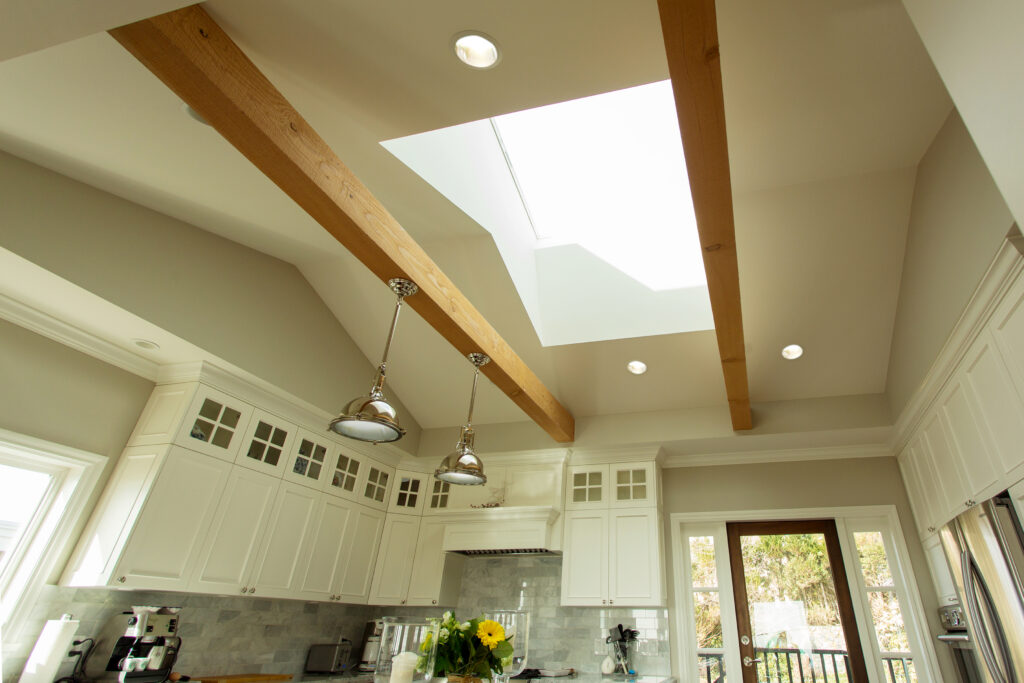 Renovated kitchen with a large skylight, vaulted ceiling, exposed wood beams, white cabinets, and pendant lighting.